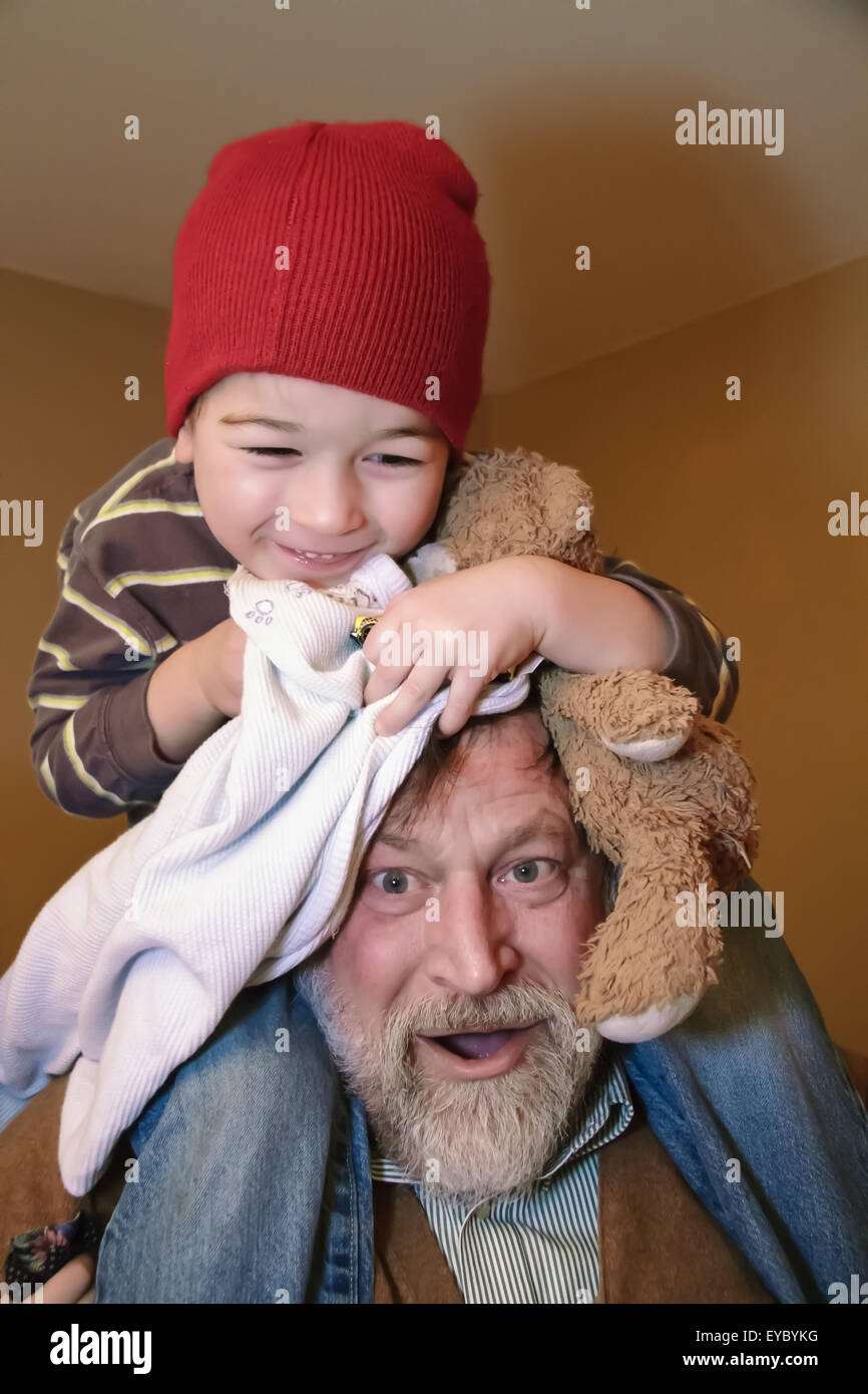 Tres años de edad cabalgando sobre los hombros de su abuelo, abrazando a su osito de peluche y una manta, en Issaquah, Washington, EE.UU. Foto de stock