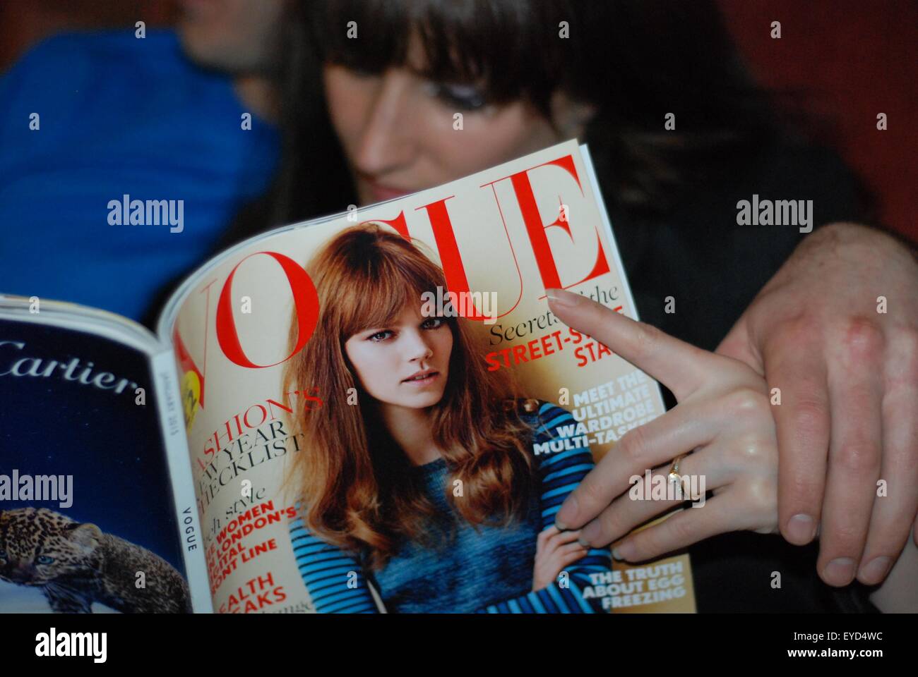 Pareja recién enganchada sujetando las manos. Está leyendo una revista Vogue. Foto de stock