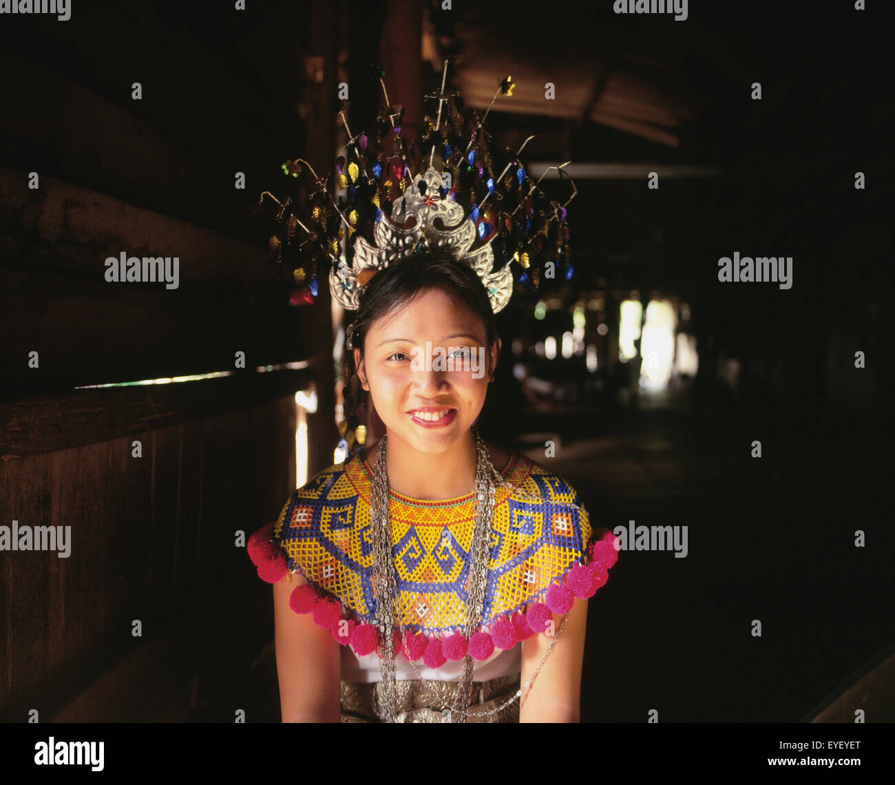 Mujer joven arrodillado en una aldea long house en traje tradicional; Sarawak Foto de stock