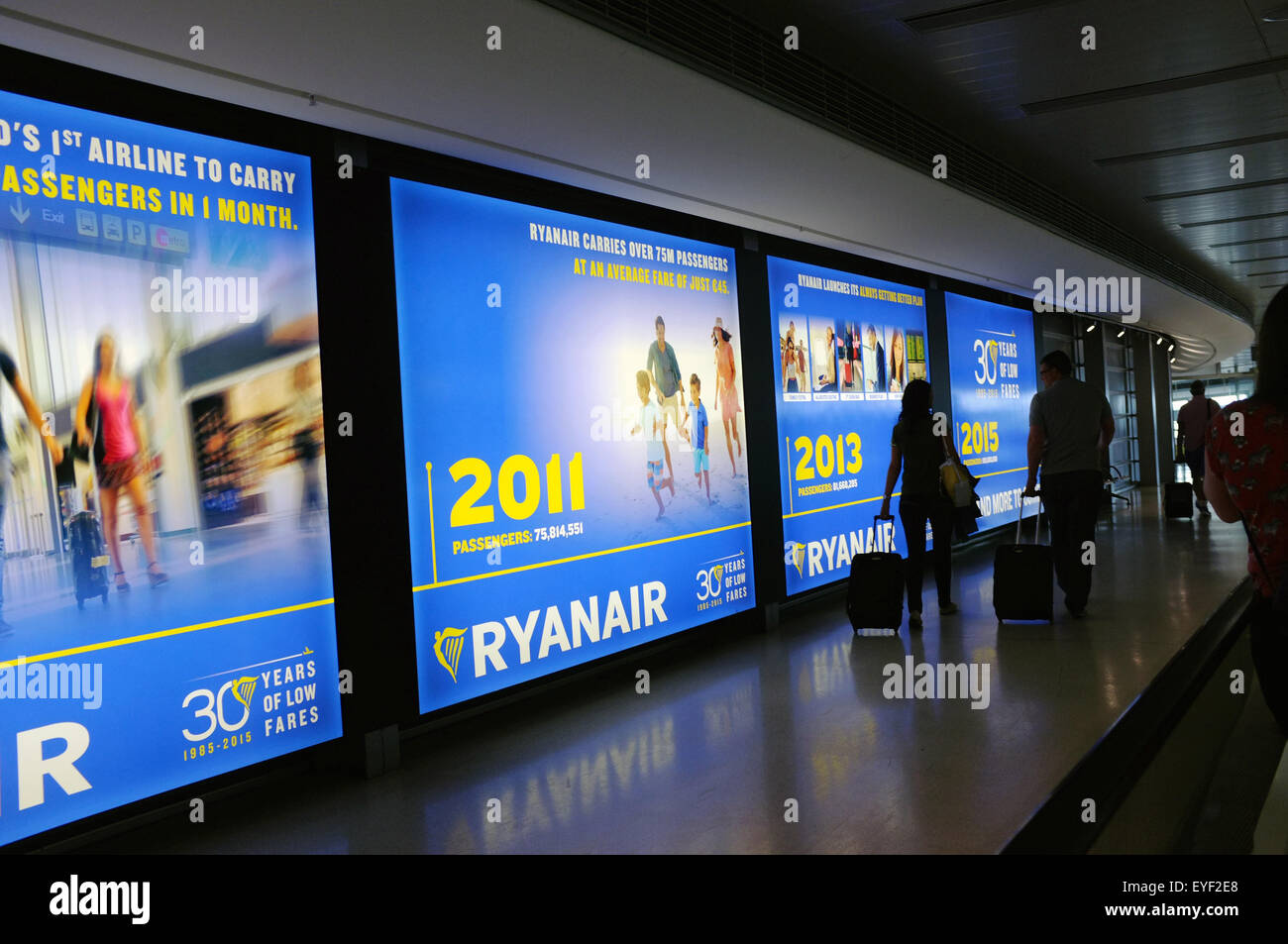 Los pasajeros atravesar una fila de Ryan Air anuncios dentro del aeropuerto de Dublín. Foto de stock