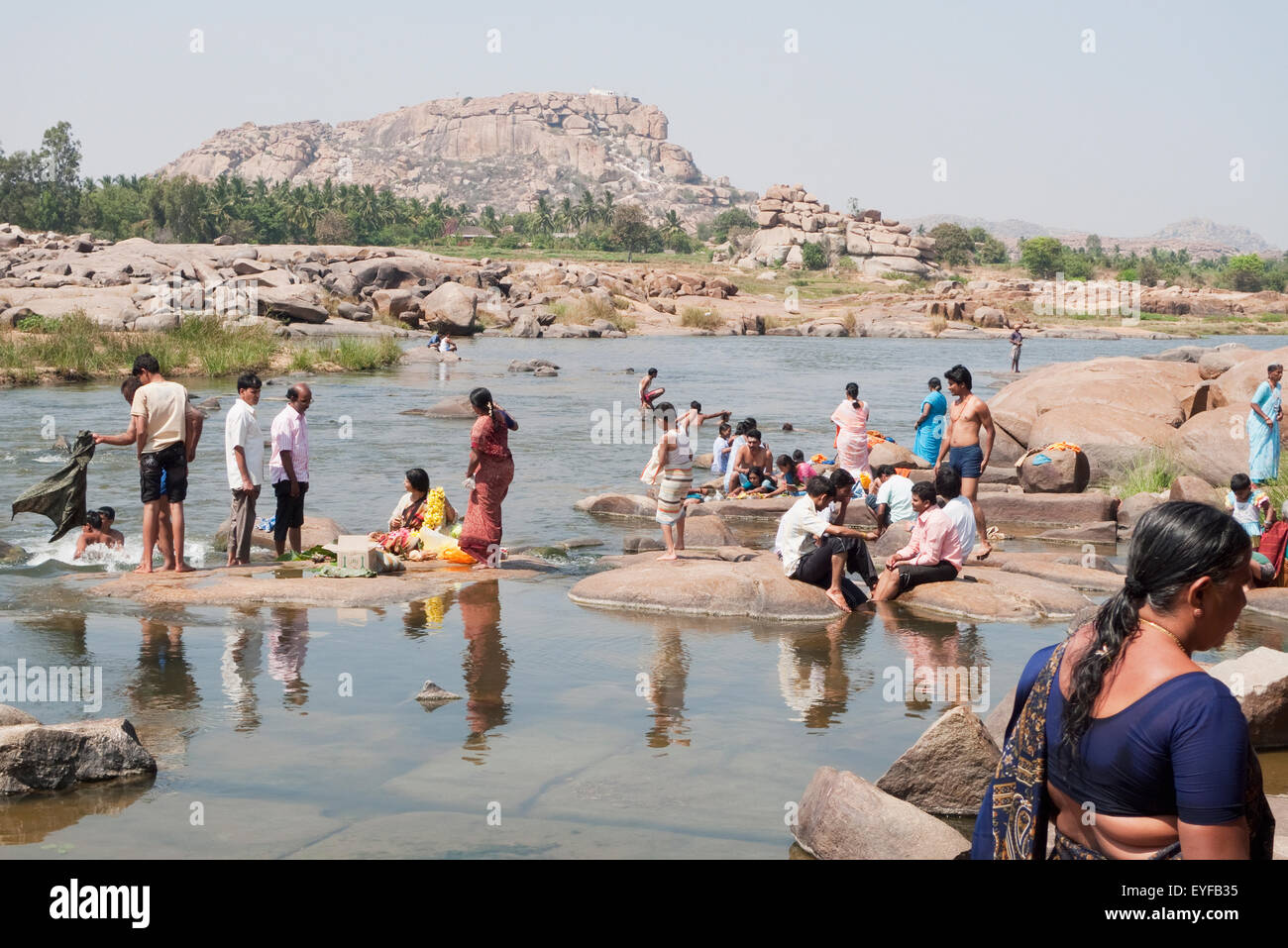 La gente a tomar un baño en el río Tungabhadra en Hampi. En la parte superior del templo de Hanuman Anjaneya Hill, en el fondo, Karnataka, India Foto de stock