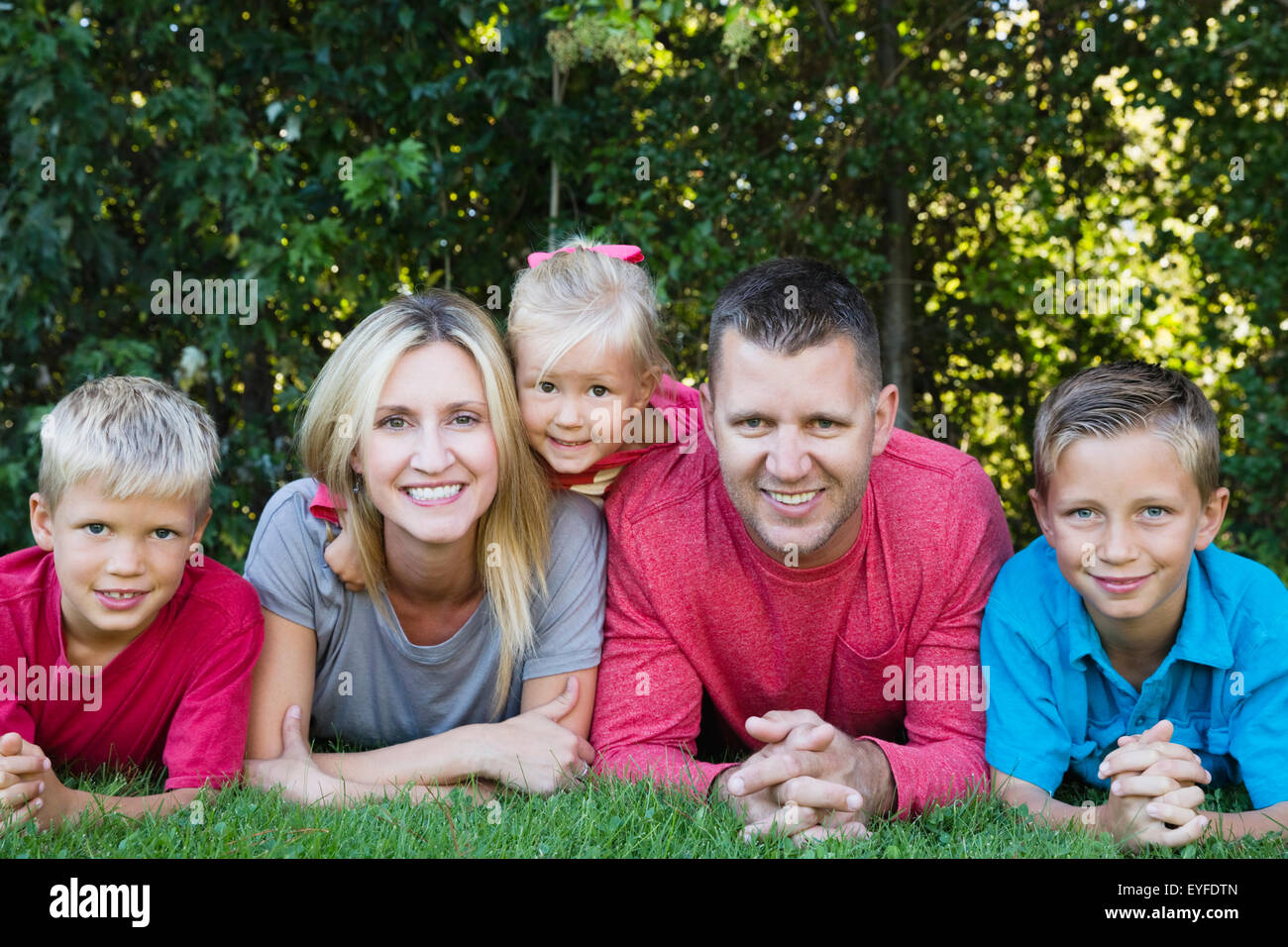 Los padres con hijos (8-9, 10-11) y su hija (2-3) tumbado sobre el césped Foto de stock