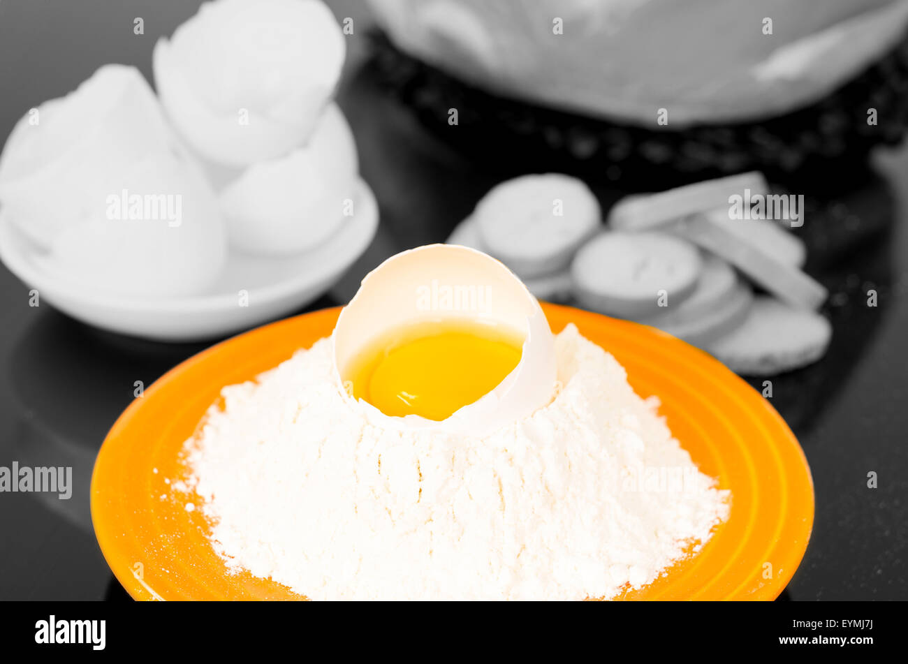 Placa de color amarillo fuerte con harina cráter que contengan huevos resquebrajados, blanco y negro alrededores disparó desde arriba ángulo lateral Foto de stock