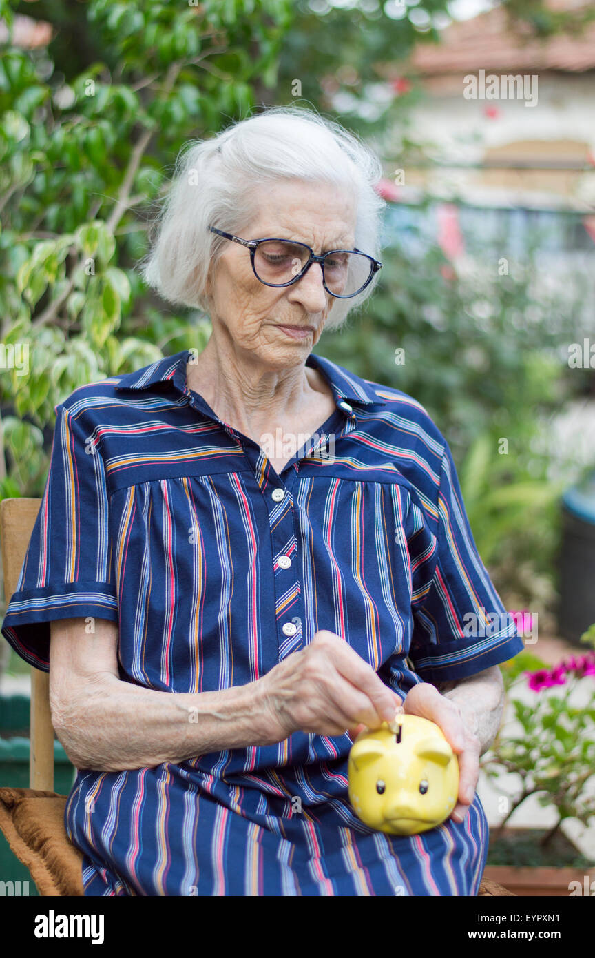 Abuela vieja ahorrando dinero de jubilación con una alcancía Foto de stock