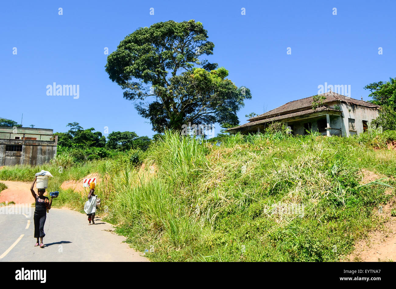 Dos mujeres cargando bolsas sobre su cabeza en la carretera por una casa abandonada en Angola Foto de stock