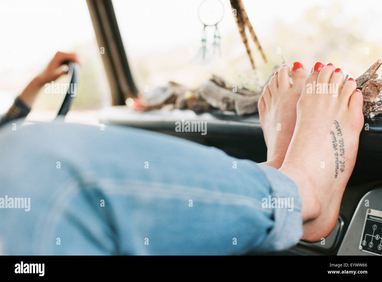 Mujer descansando sus pies descalzos en el tablero de a bordo de un 4x4, un tatuaje en su pie derecho. Foto de stock