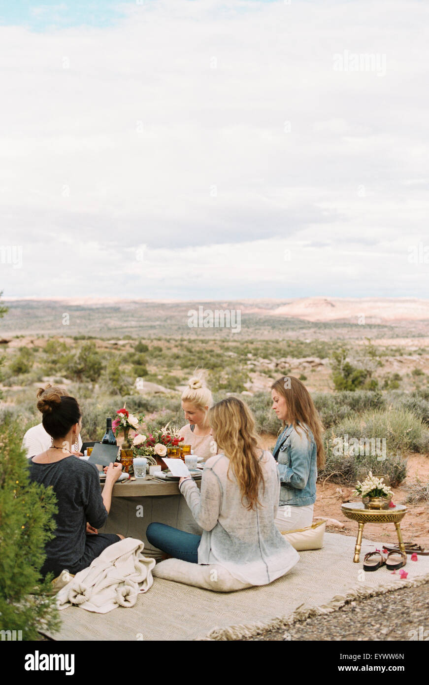 Un grupo de mujeres, amigos, sentados en el suelo alrededor de una mesa en el desierto. Foto de stock