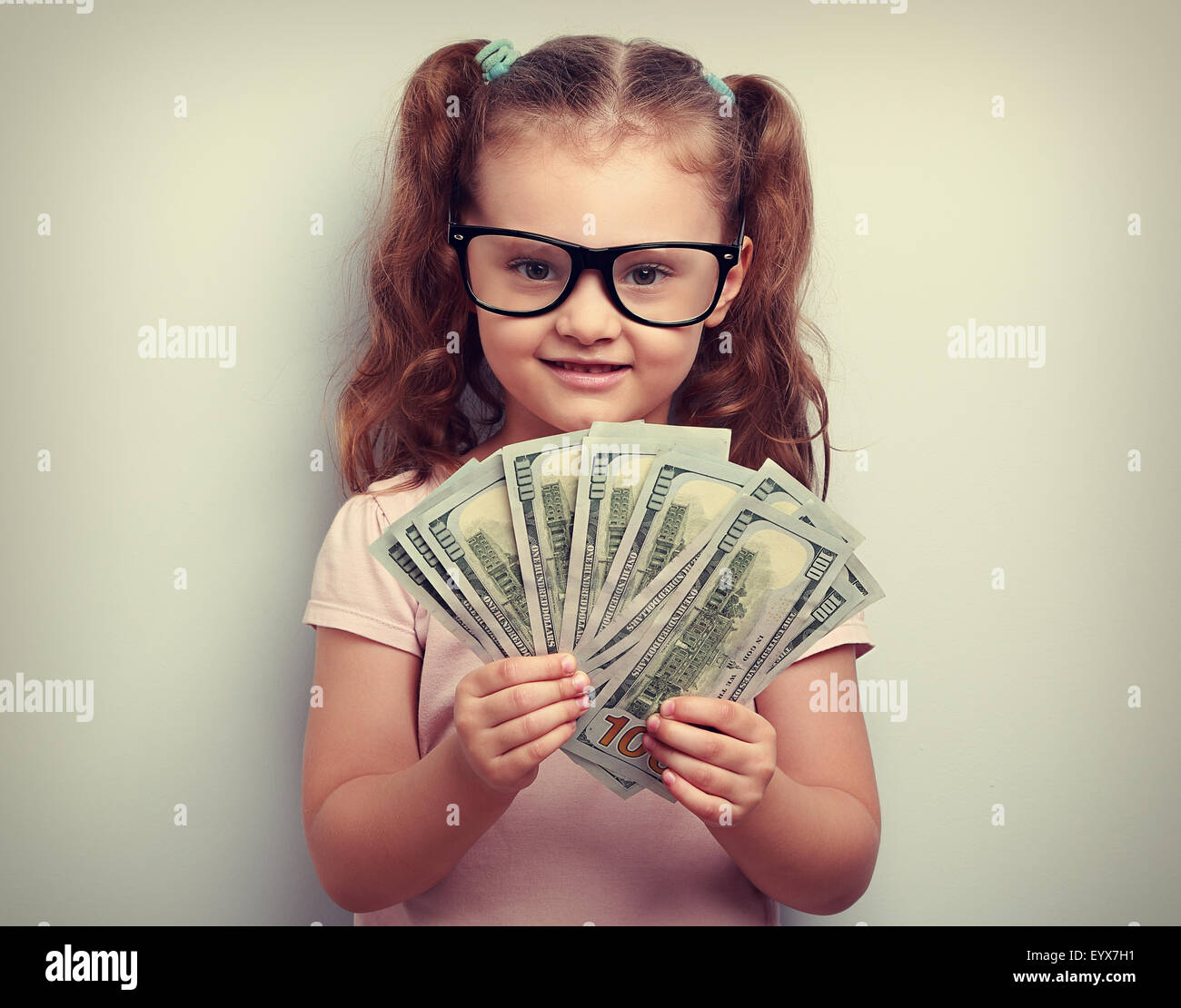 Feliz emoción kid chica en vidrios mantener dinero en la mano y mirando con una sonrisa. Vintage closeup retrato Foto de stock
