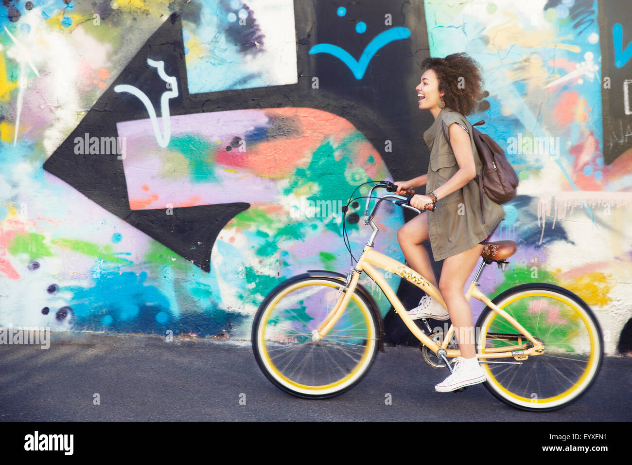 Mujer montando bicicleta por multicolor urbano graffiti wall Foto de stock