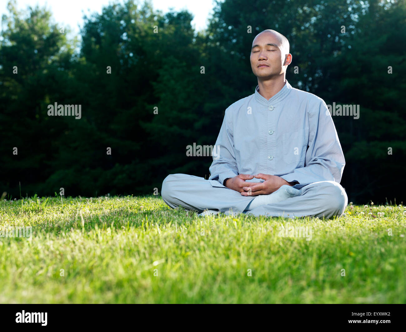 Monje Shaolin meditar al aire libre durante el amanecer sentado en el pasto verde Foto de stock