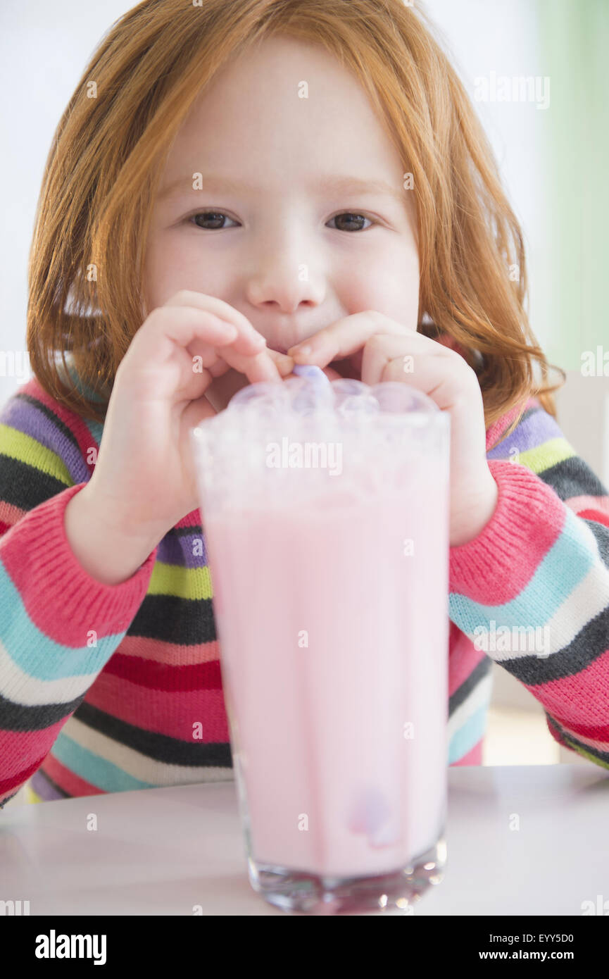 Chica caucásica soplando burbujas en leche fresa Foto de stock