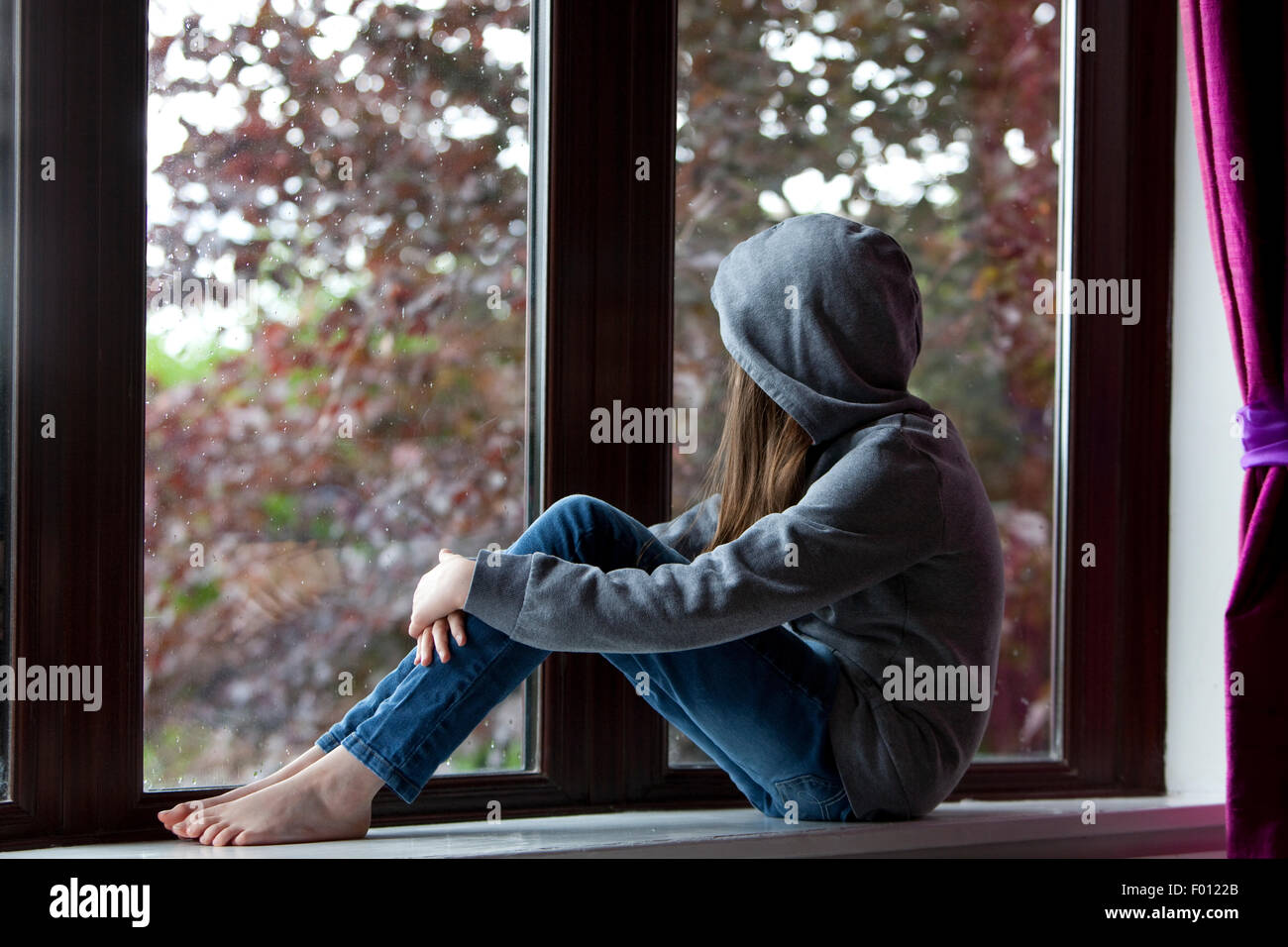 Chica en sudadera con capucha y jeans, sentada en una repisa de la ventana  interior y mirar hacia el exterior Fotografía de stock - Alamy