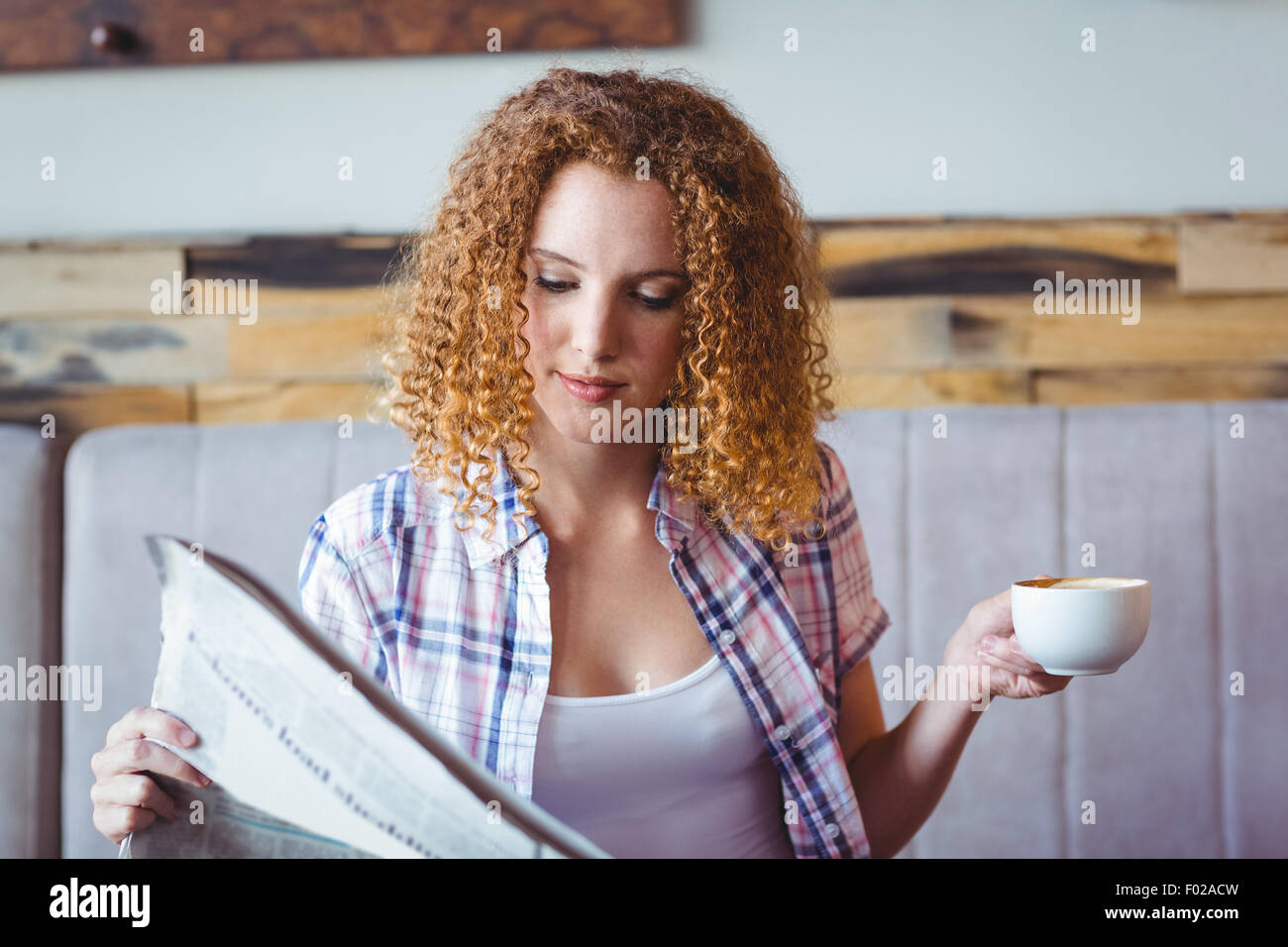 Bonita chica de cabello rizado con la taza de café y leyendo el periódico Foto de stock