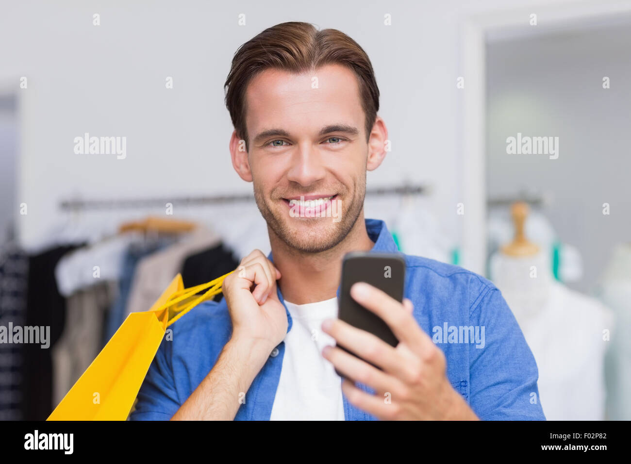 Un hombre sonriente con bolsas de compras busca en su smartphone Foto de stock