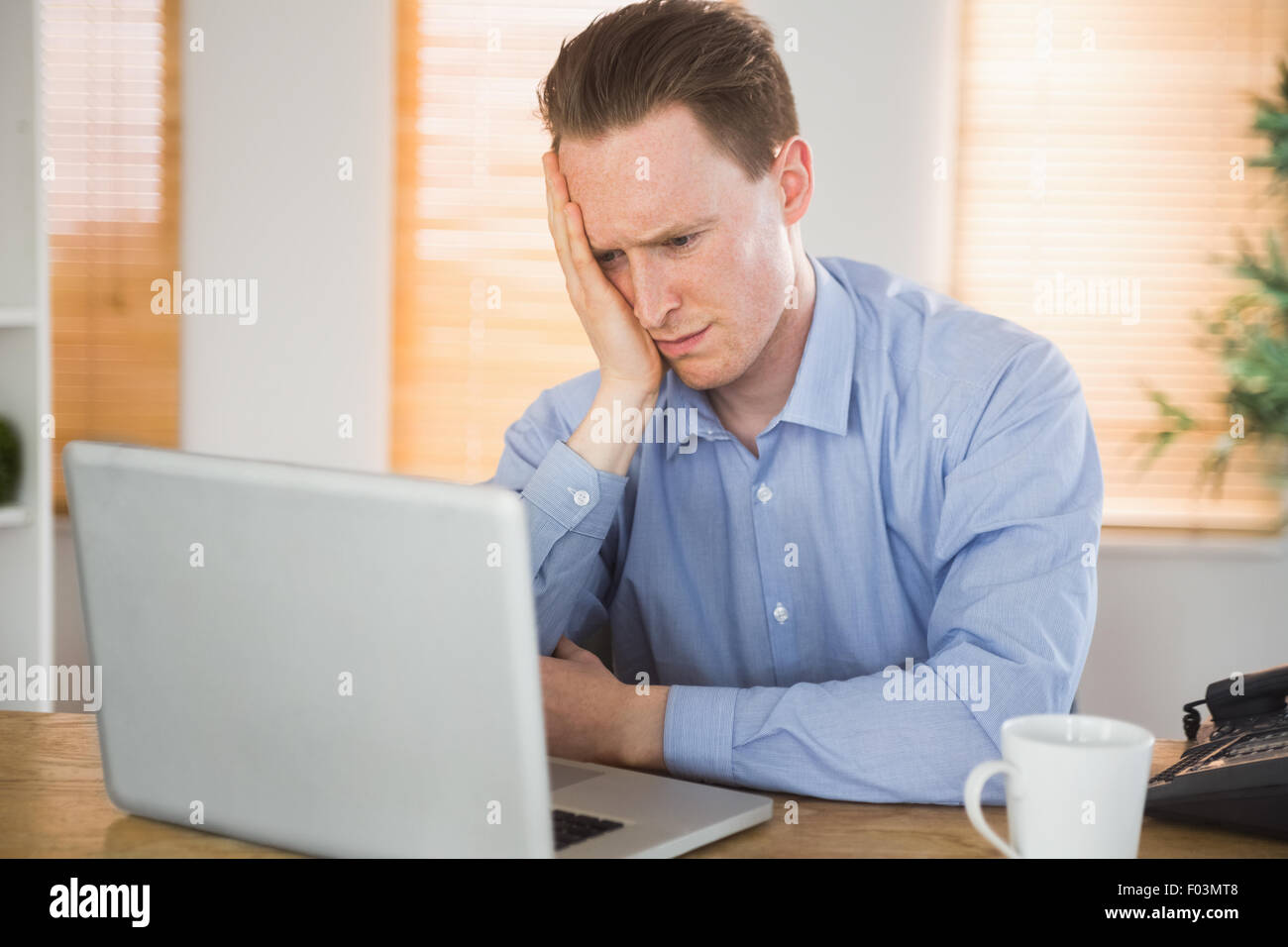Empresario temeroso mirando a su portátil. Foto de stock