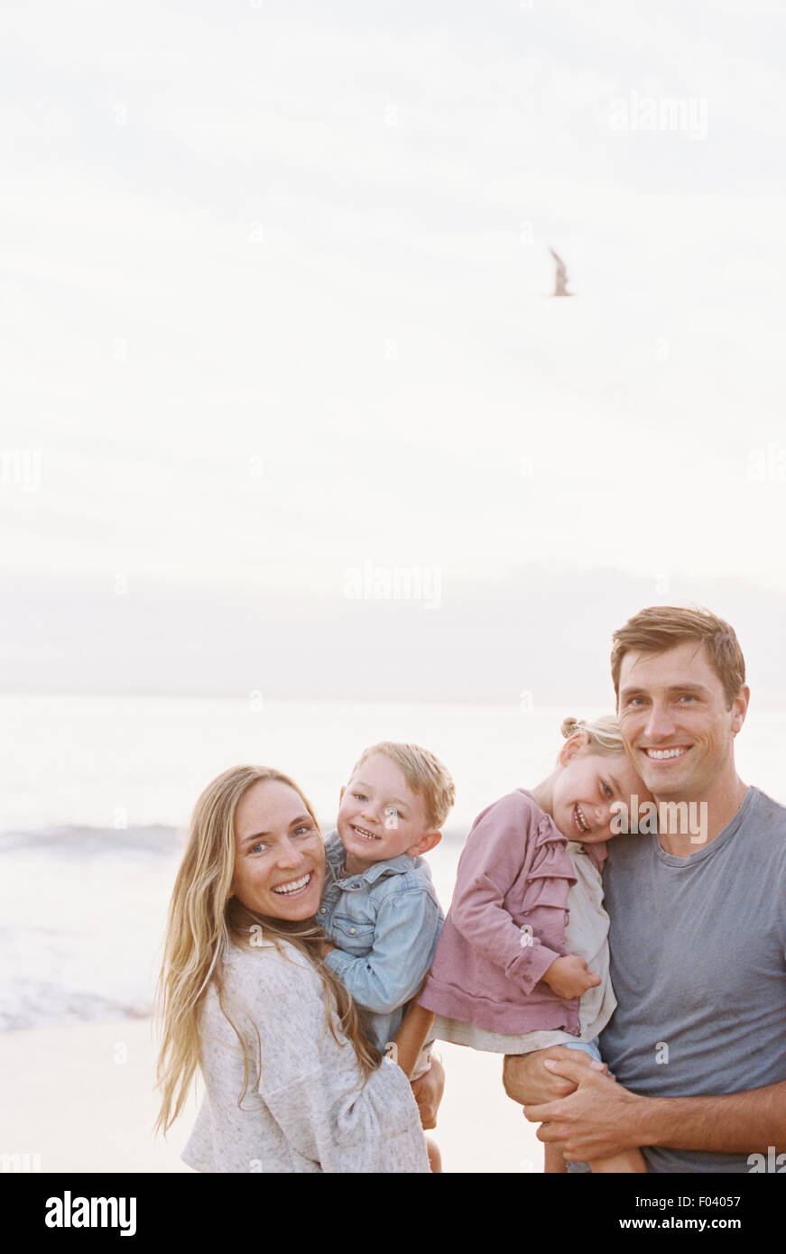 Par de pie con su hijo e hija en una playa de arena a la orilla del mar, mirando a la cámara, sonriendo. Foto de stock