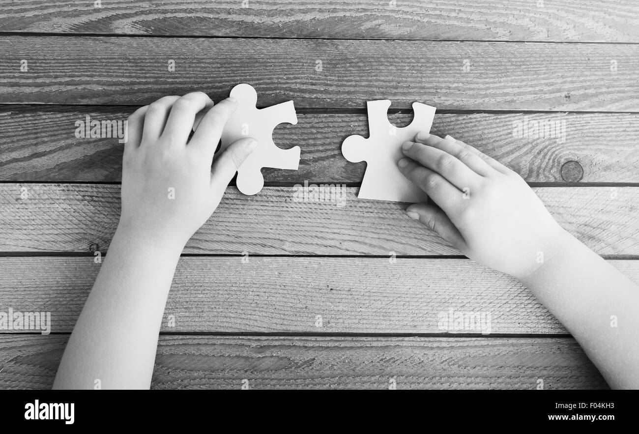 Imagen recortada de manos conectando dos piezas de un rompecabezas sobre la mesa de madera, fotografía en blanco y negro Foto de stock