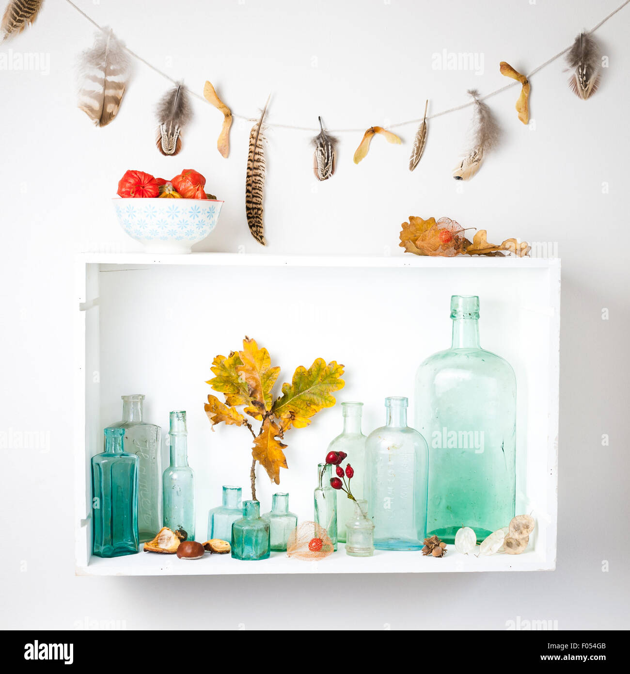 Un estante con una colección de botellas de vidrio vintage y reuniones de otoño, y la guirnalda de plumas Foto de stock