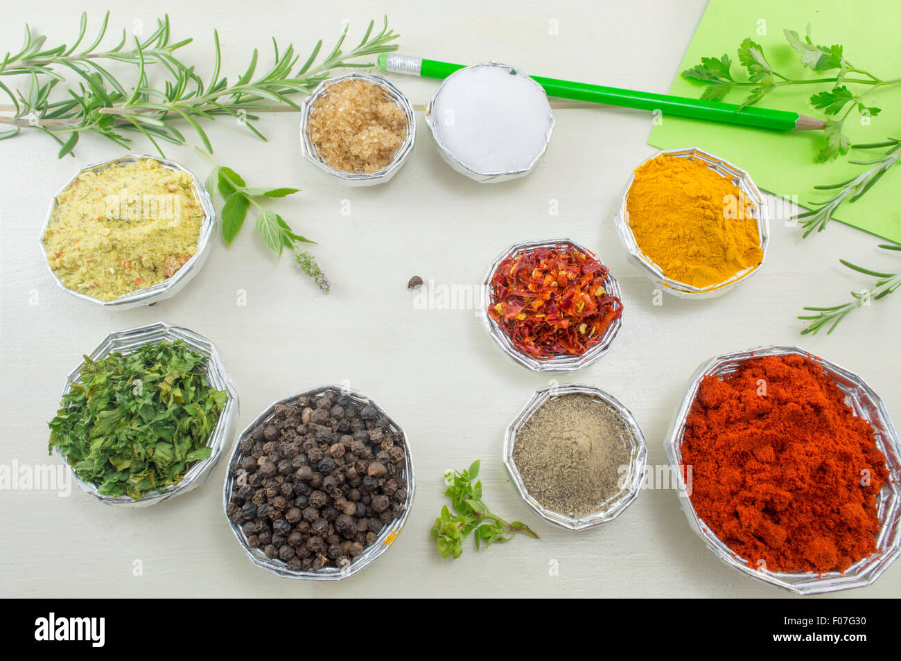 Conjunto de diferentes especias en el brillante cuencos con papel y lápiz para escribir recetas sobre una tabla de madera blanca Foto de stock