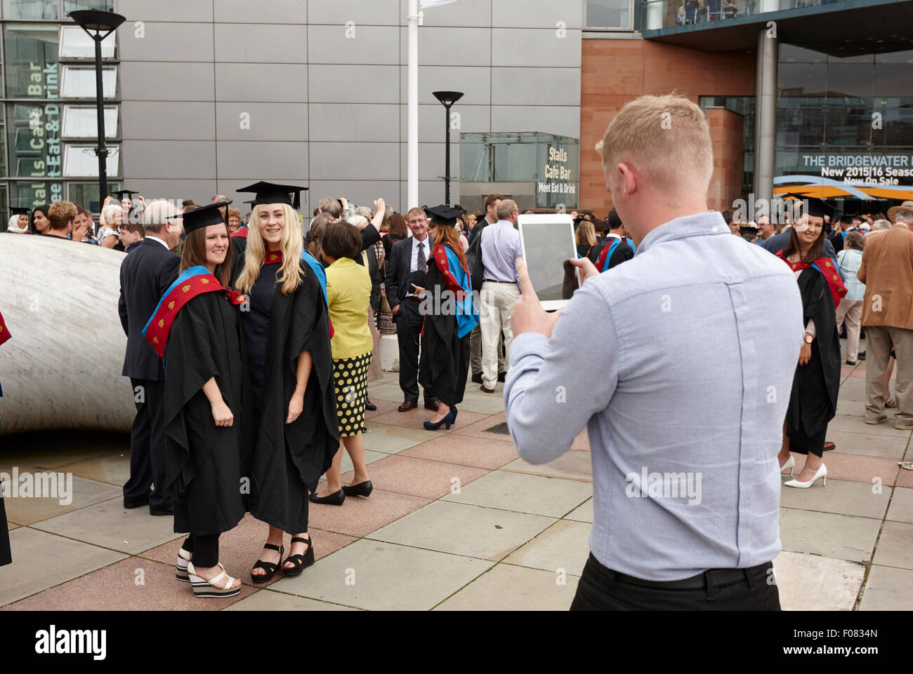 Hombre utilizando equipo de tableta para tomar fotos de las graduadas después de la ceremonia de graduación de la Universidad Metropolitana de Manchester en el hombre Foto de stock