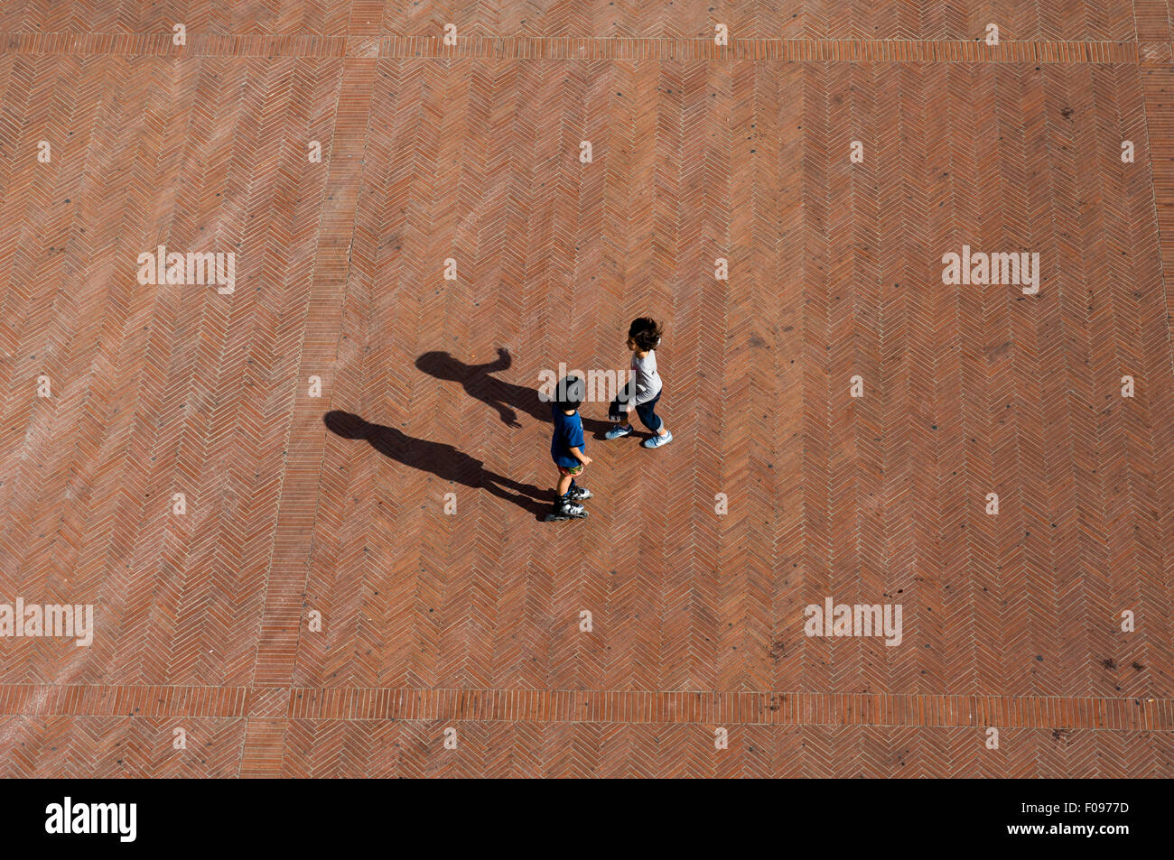 Montepulciano, Toscana, Italia. Dos niños juegan en una plaza con espina de pez rojo ladrillo pavimentación. Foto de stock