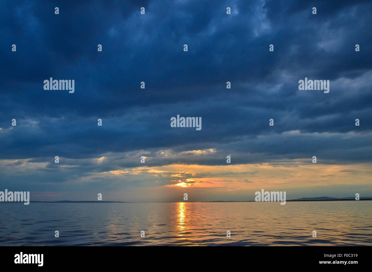 Una puesta de sol sobre el Lago de Constanza con la costa a lo lejos, las nubes oscuras y ondeando las olas Foto de stock