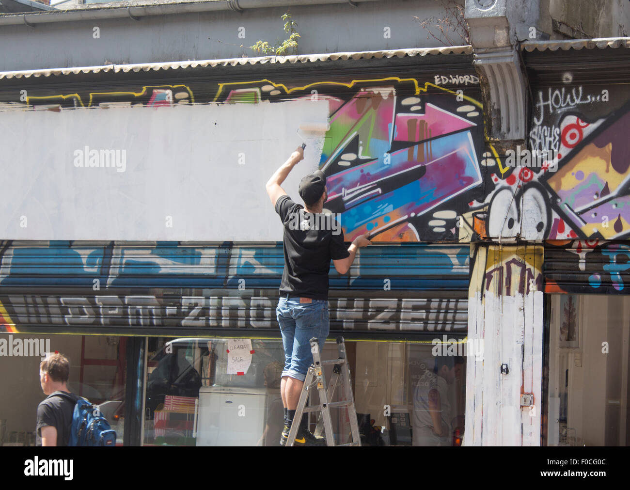 El hombre pintando encima de la eliminación de los grafitos con rodillo y pintura blanca de Brixton Londres England Reino Unido Foto de stock