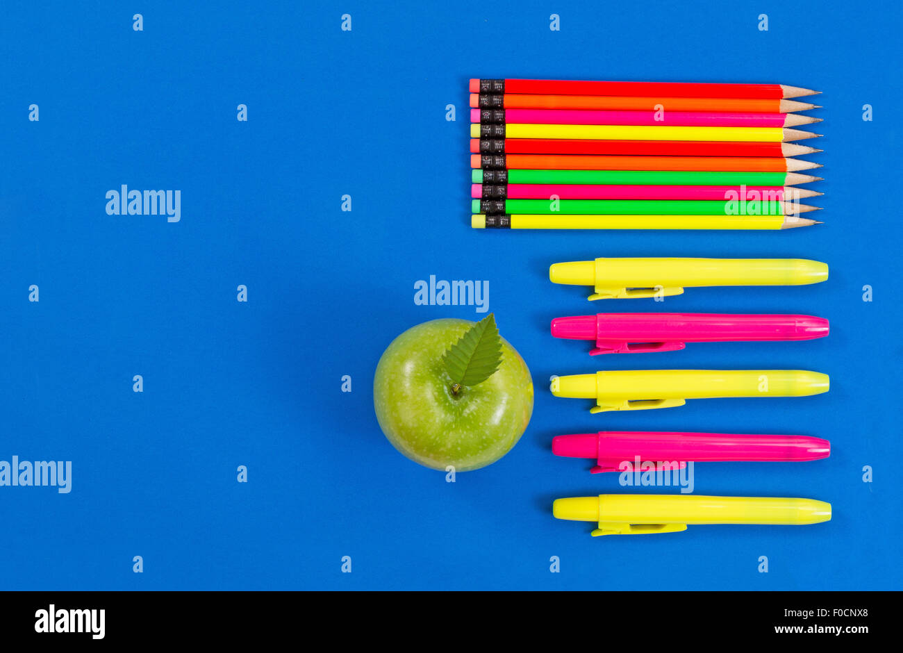 Oficina o back to school suministros consistentes en una manzana verde, resaltar los marcadores y lápices de colores sobre fondo azul. Foto de stock