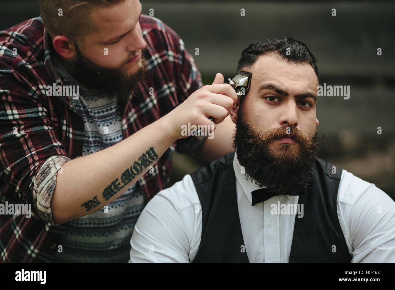 Hombre caucásico tratando de afeitarse la cabeza con una afeitadora  eléctrica. Un hombre brutal calvo sostiene una navaja en su mano y afeita  la barba sobre un fondo metálico Fotografía de stock 