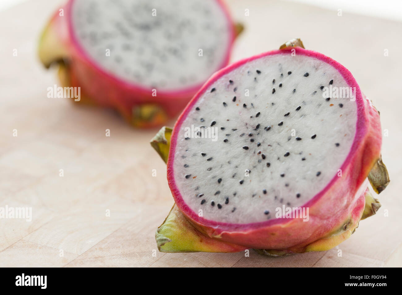 Un dragon fruit en rodajas sobre una superficie de madera fotografiado con la luz de la ventana. Foto de stock