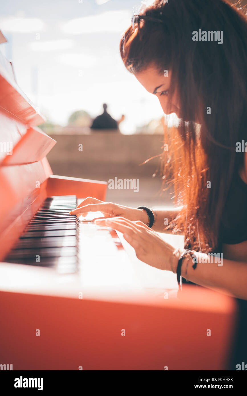 Cerca de una hermosa joven de cabello marrón rojizo chica caucásica tocando el piano - creativo, performance, música concepto - ella está vestido con una camisa negra y juega un piano rojo Foto de stock