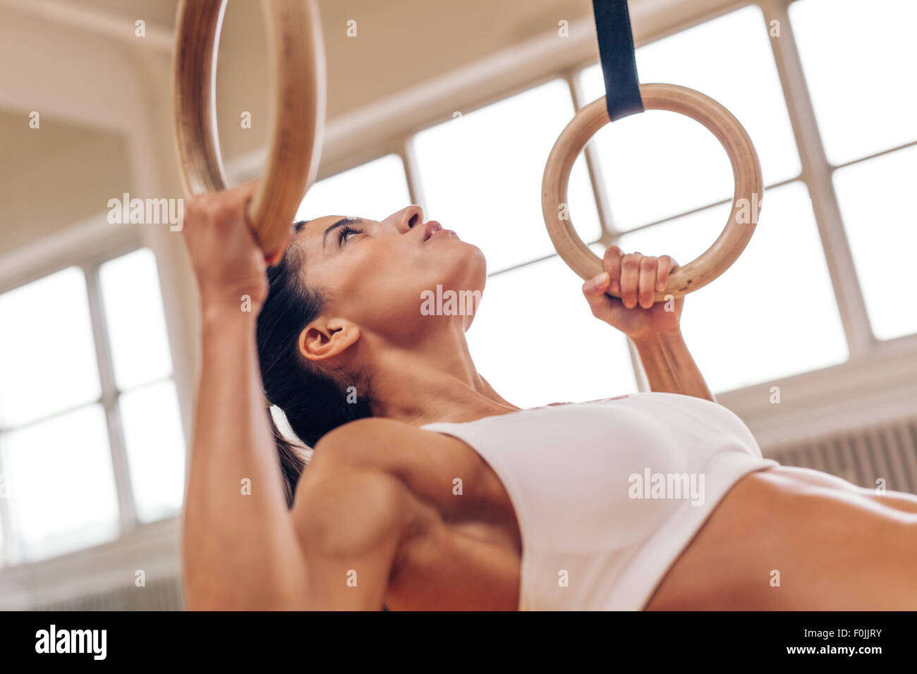 Primer plano de fuerte joven haciendo pull-ups con anillos de gimnasia. La atleta femenina de Fitness ejercicio en el gimnasio. Foto de stock