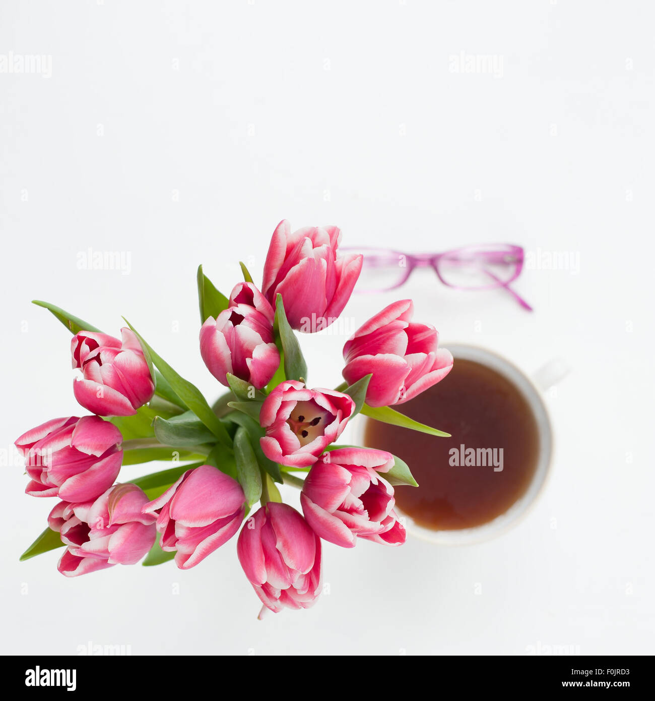 Un Ramo de tulipanes rosa brillante con taza de té borrosa y vasos en el fondo Foto de stock