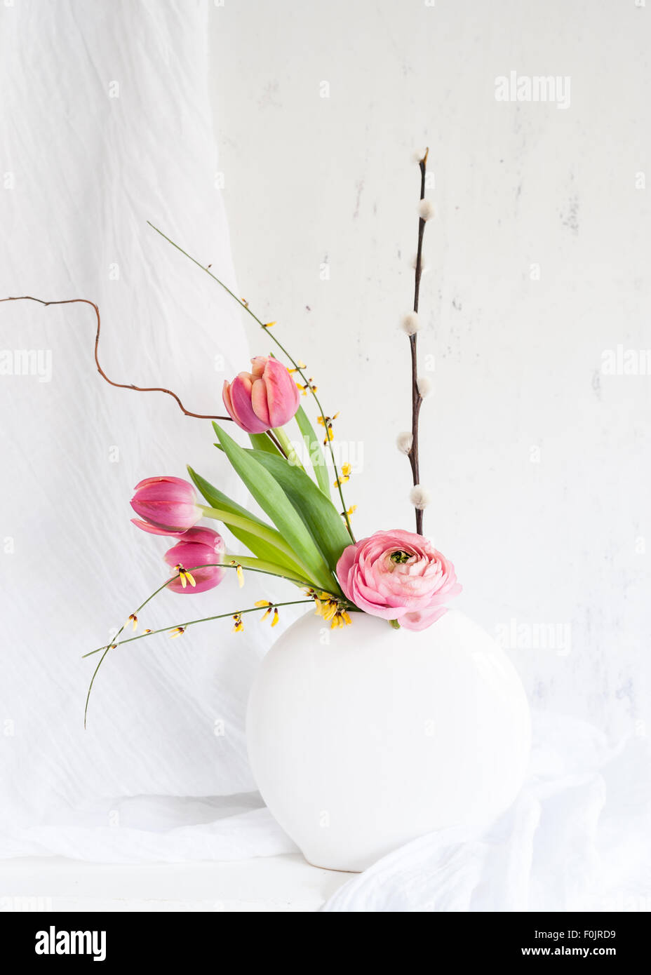 Una simple flor arreglos de tulipanes rosados, ranunculus, amarilla genista y ramitas de sauce en un jarrón redondo Foto de stock