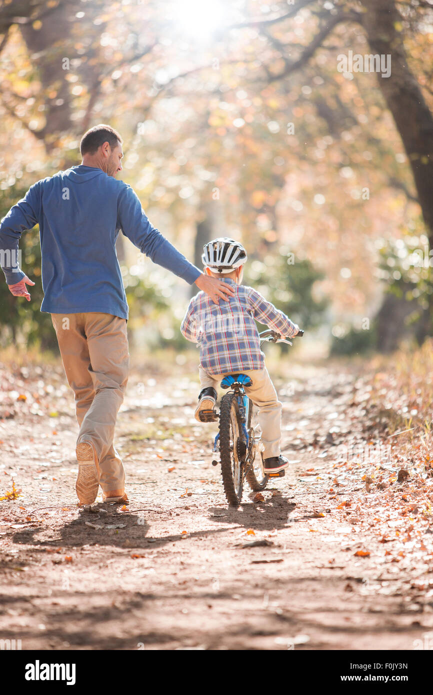 Padre enseñar al hijo a andar en bicicleta en la ruta en maderas Foto de stock
