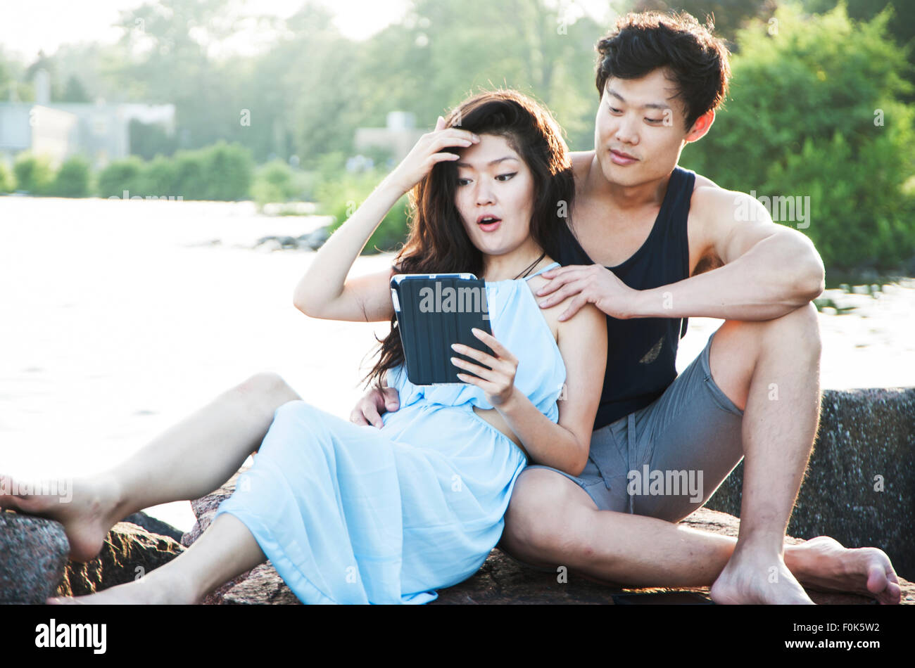 Pareja asiática sentado afuera con mujer leyendo desde un lector de correo electrónico Foto de stock