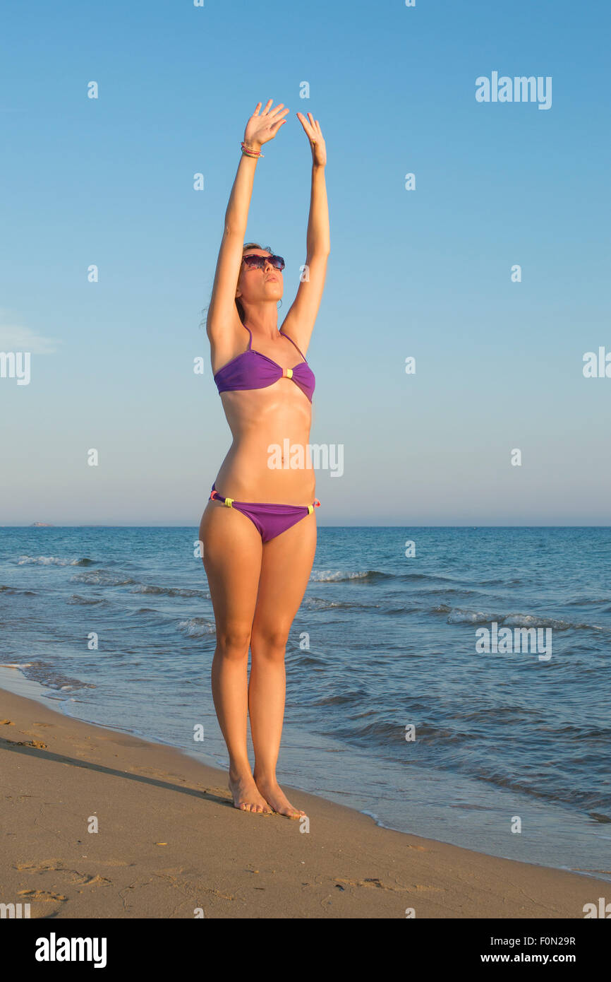 Chica en Bikini y el ejercicio de estiramiento en la playa mirando el atardecer Foto de stock