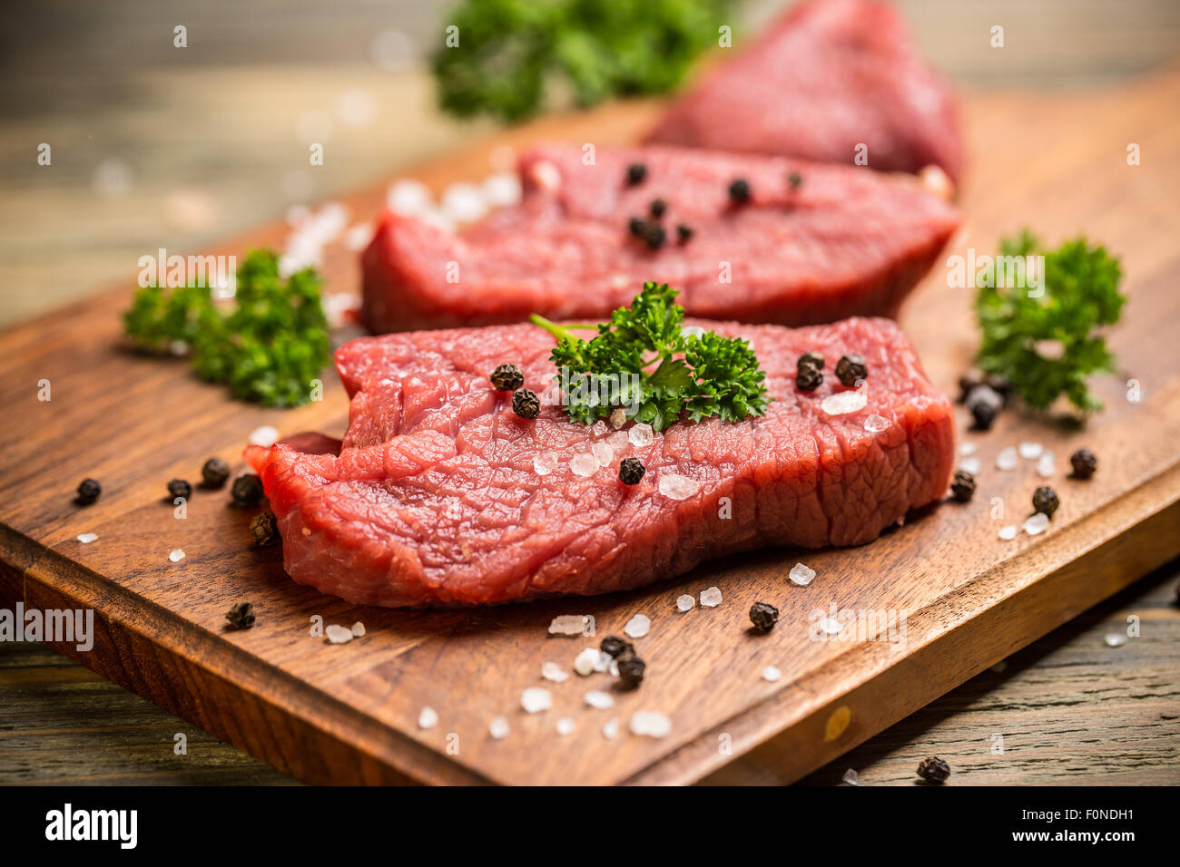 Carne fresca cruda sobre la tabla de cortar de madera con perejil, sal y pimienta Foto de stock