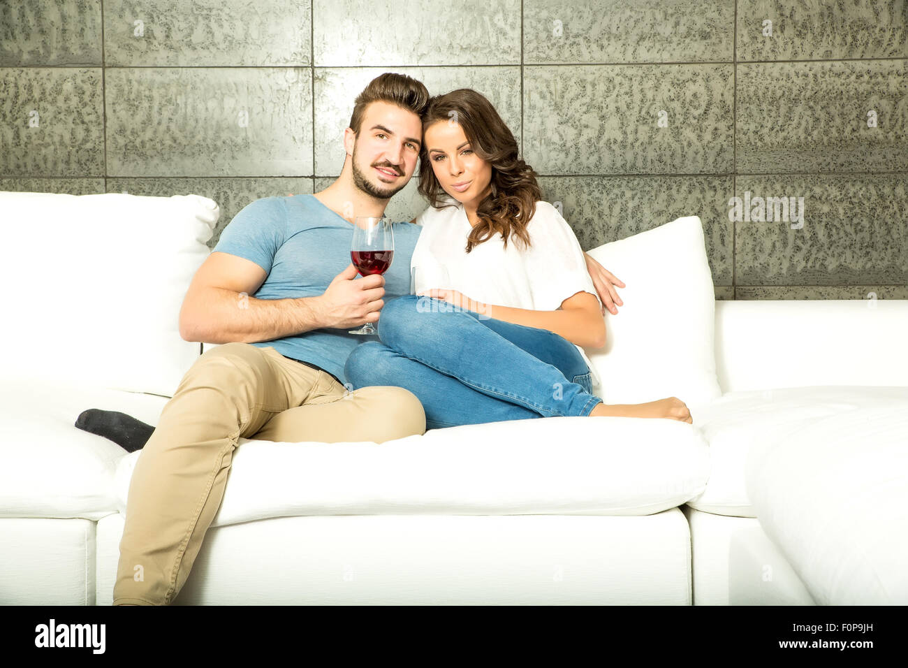 Una joven pareja en la sala de estar disfrutando de una copa de vino tinto  en el sofá Fotografía de stock - Alamy