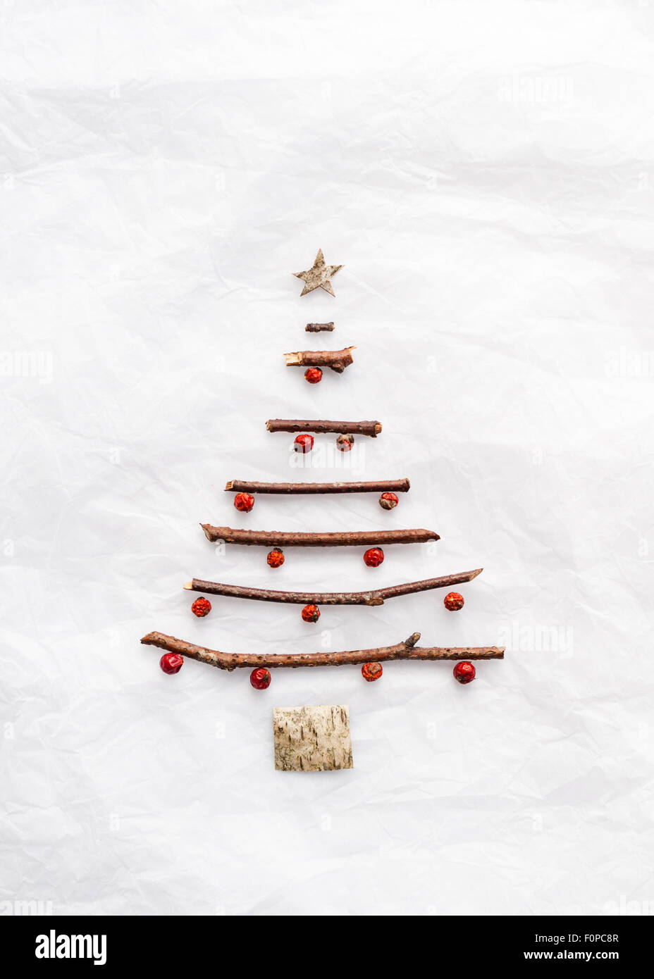 Una simple forma de árbol de Navidad hecho con ramitas de abedul corteza y bayas rojas en papel de tejido fino blanco Foto de stock