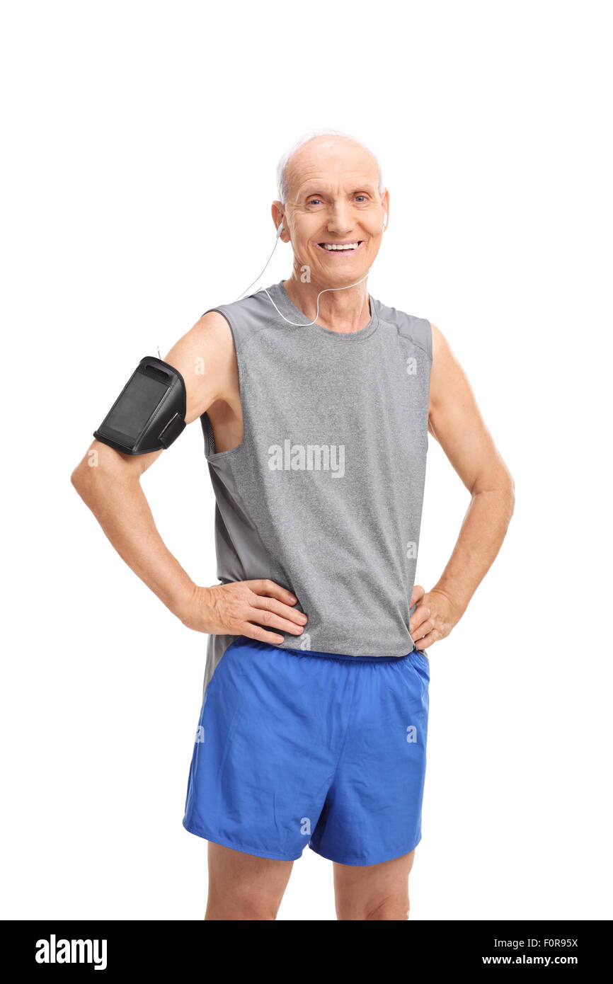 Foto de estudio de un hombre senior en ropa deportiva escuchando música en su teléfono celular y mirando la cámara Foto de stock