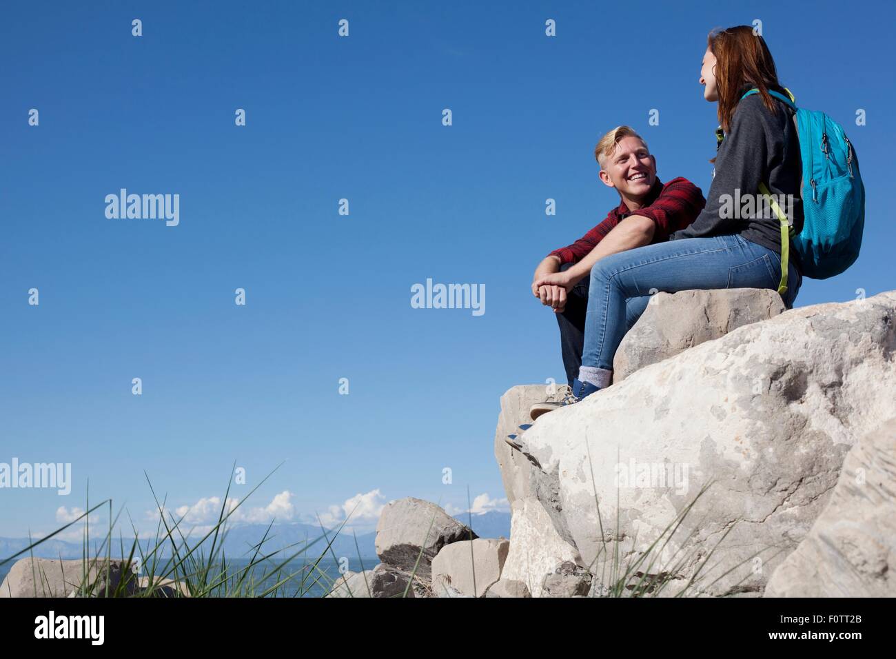 Ángulo de visión baja de la joven pareja sentada sobre las rocas sonriendo Foto de stock