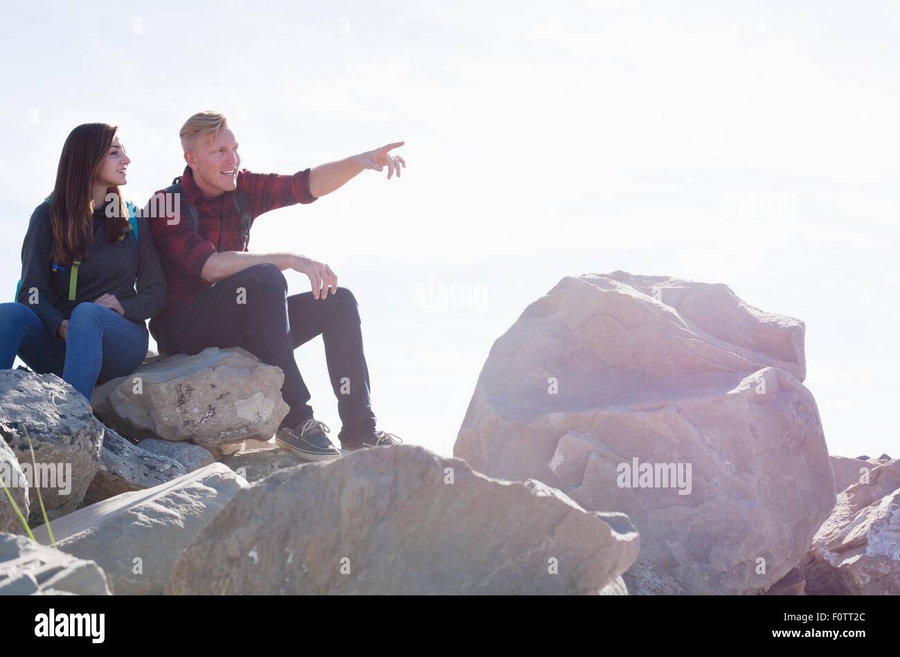 Pareja joven sentada sobre las rocas en busca de distancia apuntando Foto de stock