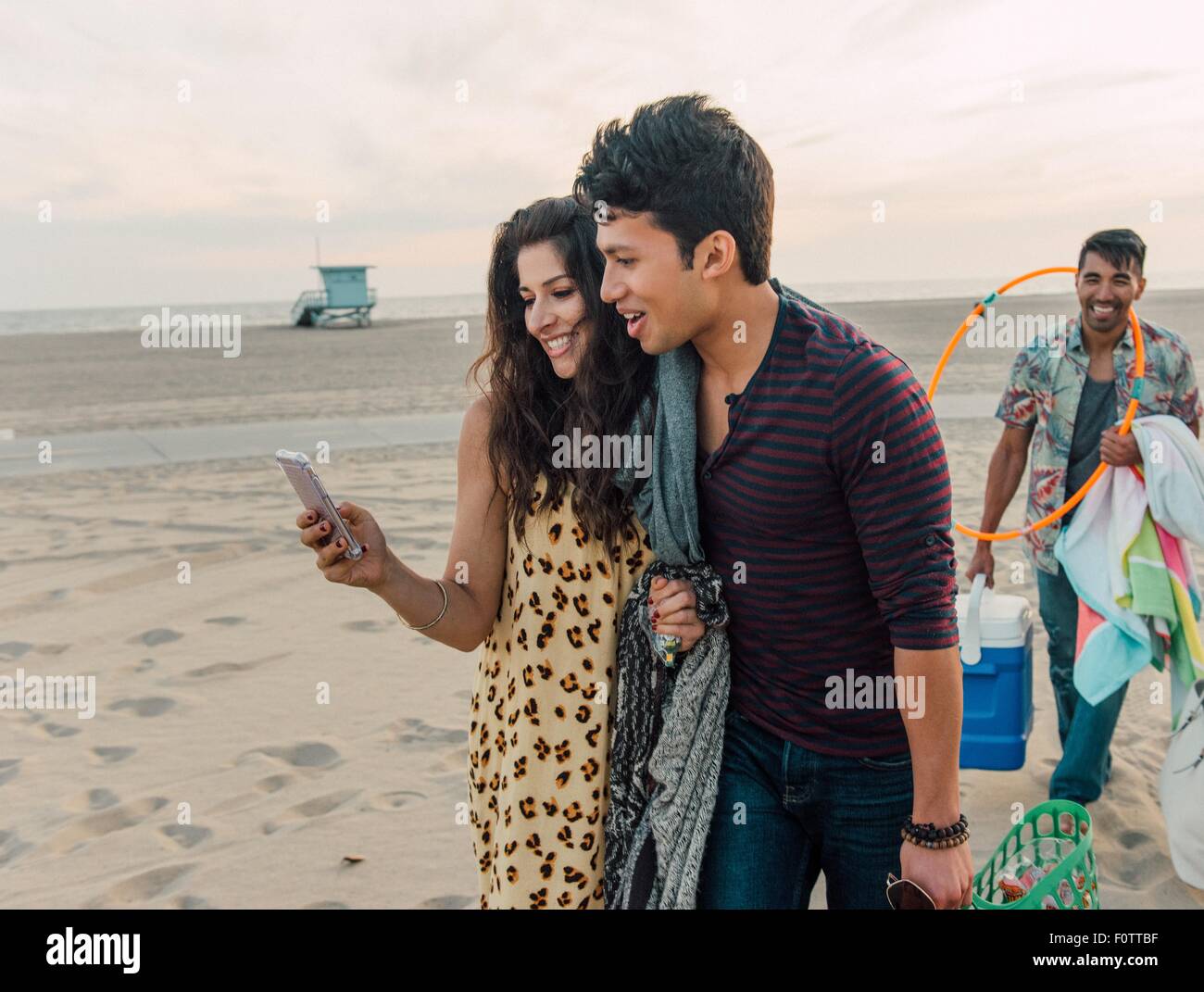 Grupo de amigos caminando por la playa, joven pareja mirando el smartphone Foto de stock