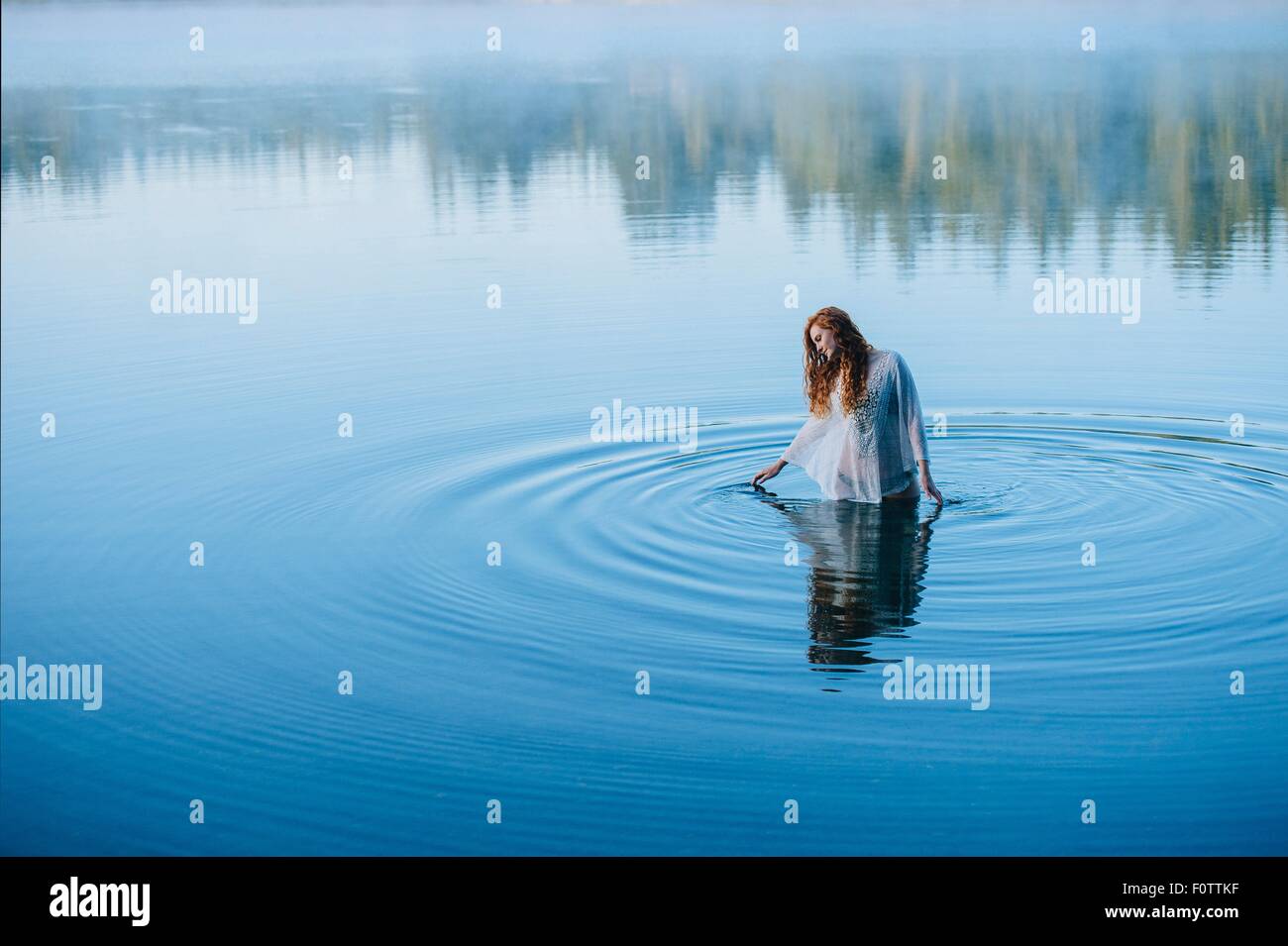 Mujer joven de pie en medio del lago ripples mirando hacia abajo Foto de stock