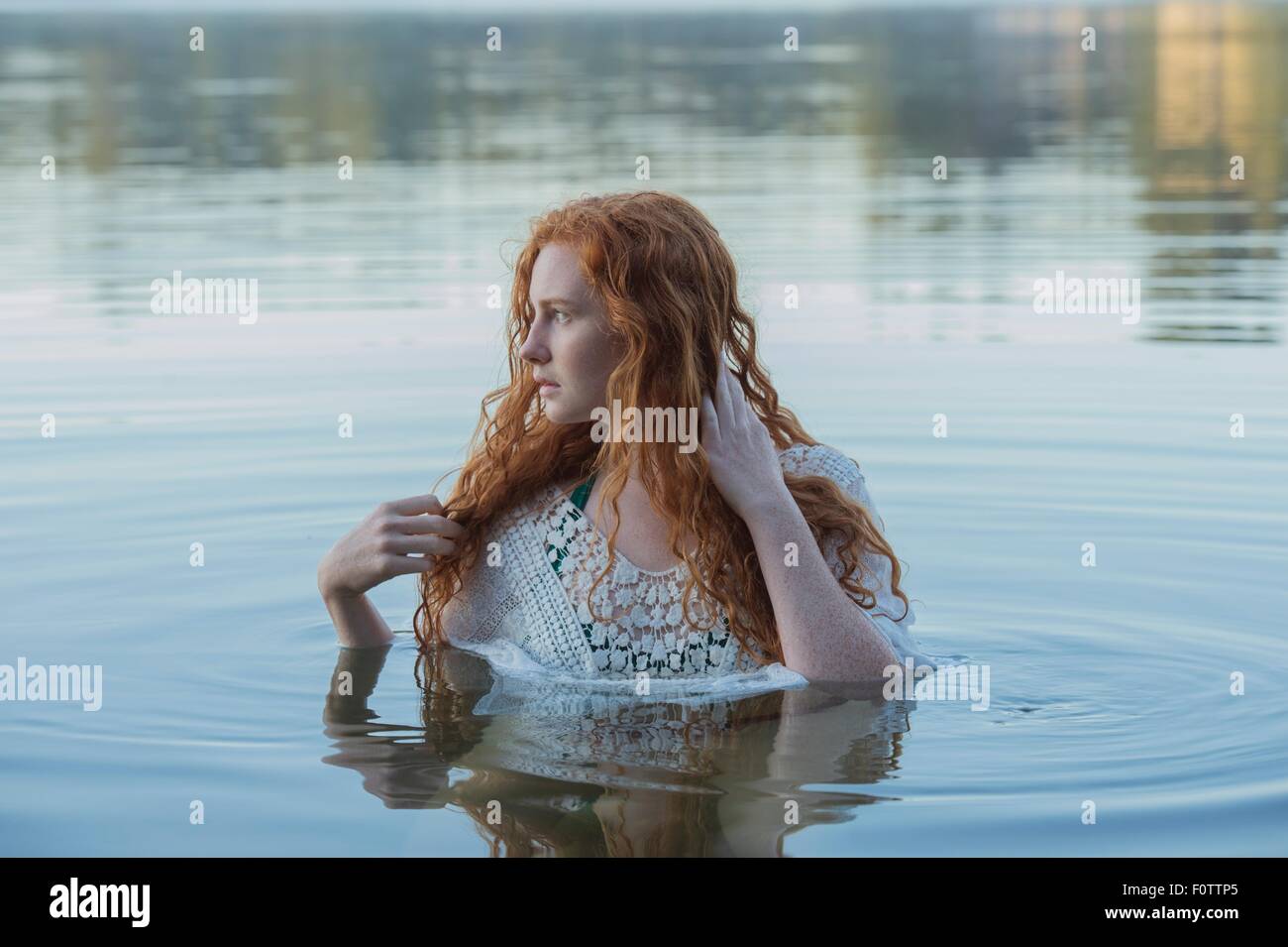 Cabeza y hombros de la mujer joven con largo pelo rojo en el lago mirando lateralmente Foto de stock