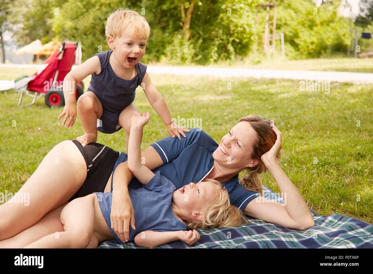 Madre e hijos relajante en estacionamiento, mintiendo en manta para picnic Foto de stock