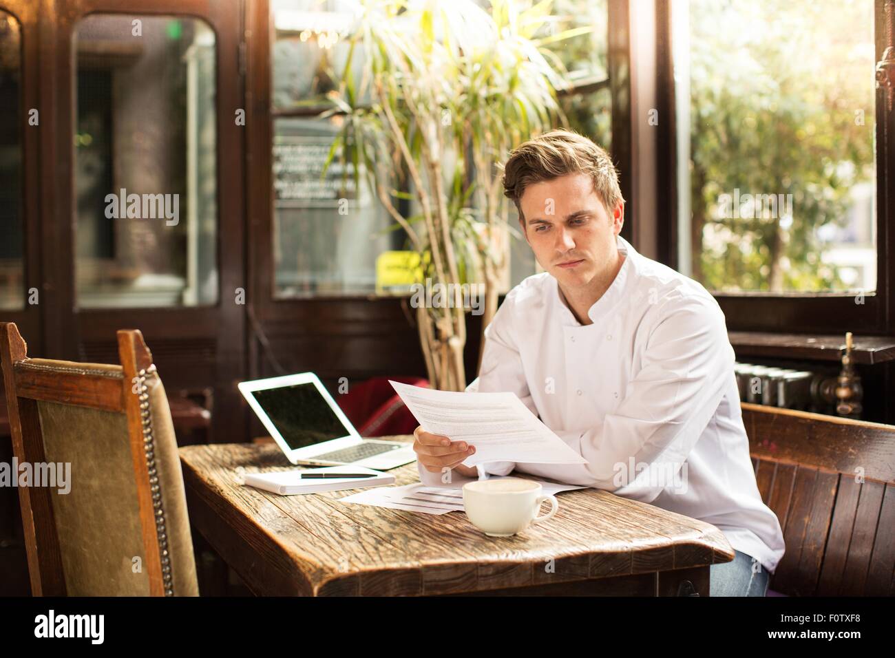 El joven chef sentado en trabajo buscando papeleo Foto de stock