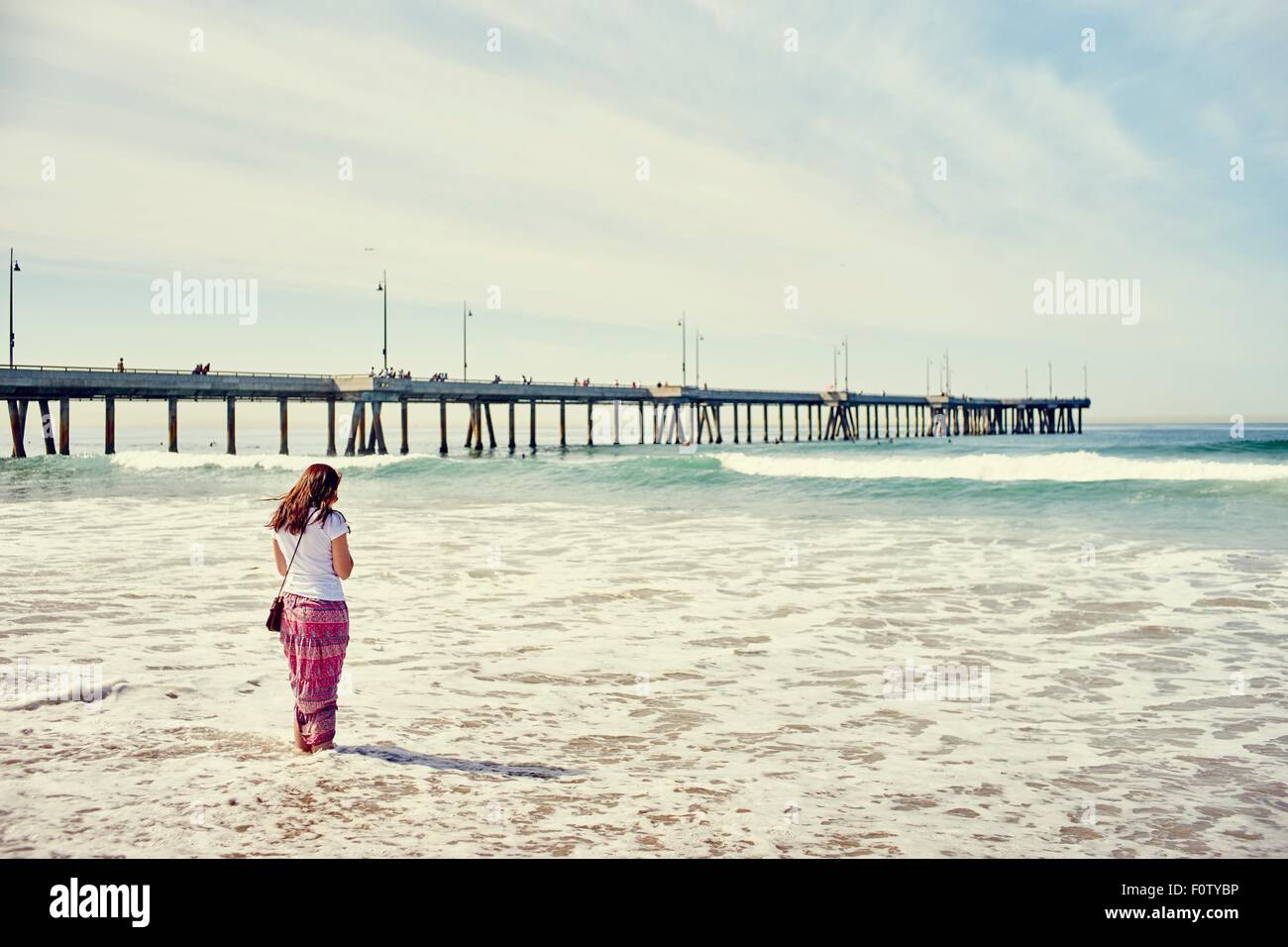 Vista trasera de la mujer remando enfrente del muelle, Venice Beach, Los Angeles, California Foto de stock