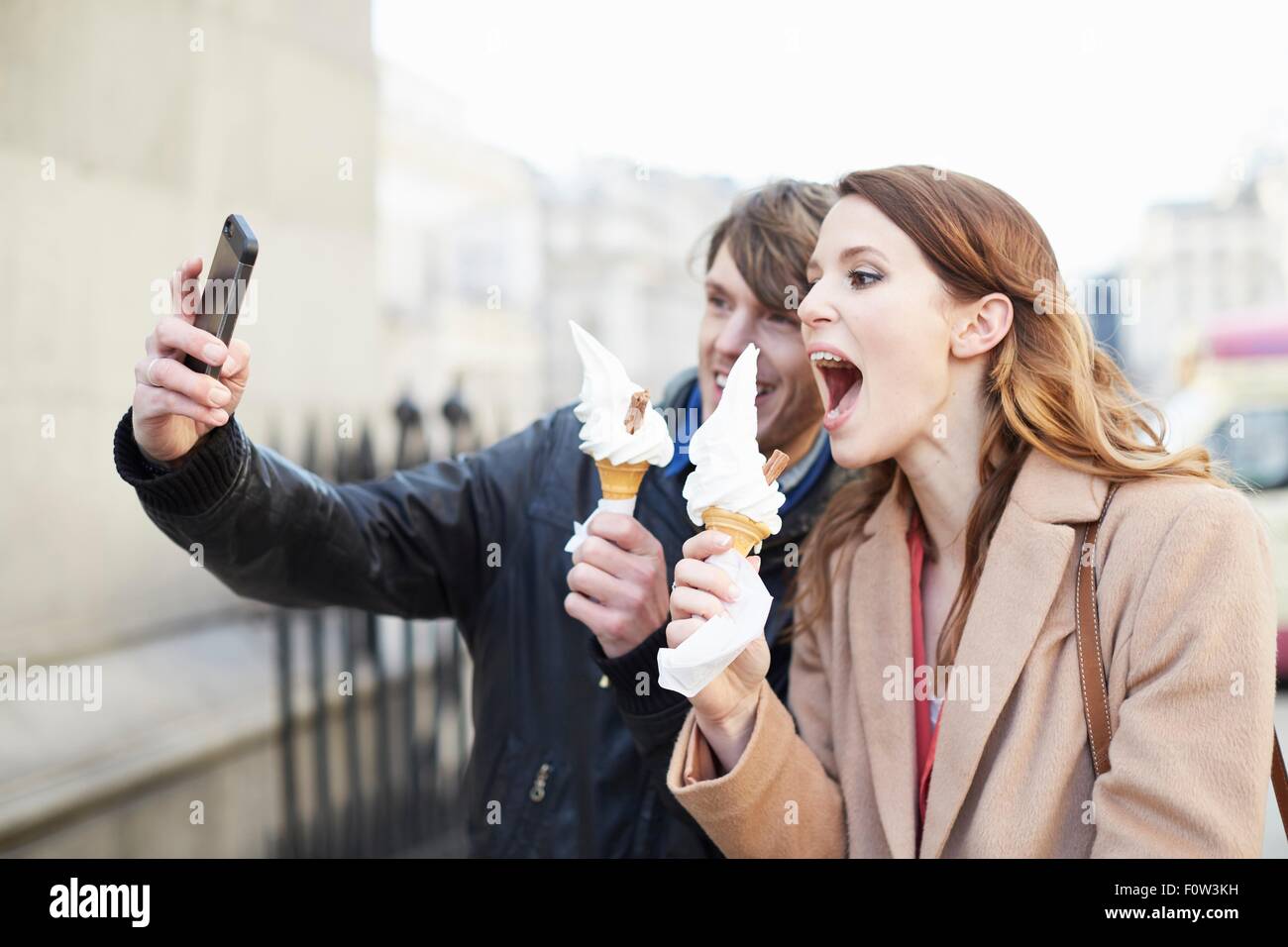 Pareja con conos de helado tomando selfie smartphone, Londres, Reino Unido. Foto de stock